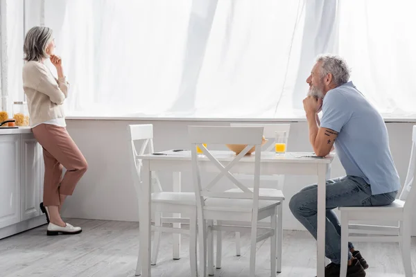 Зрелый мужчина смотрит на задумчивую жену на кухне — стоковое фото