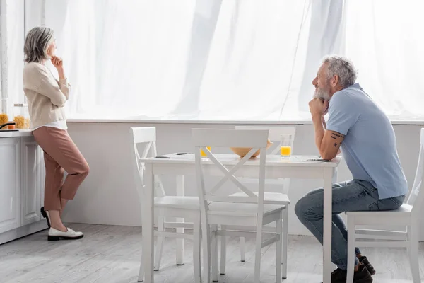 Maturo uomo guardando pensoso moglie in cucina — Foto stock