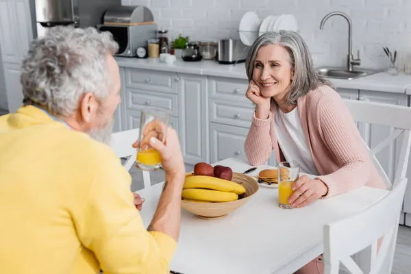 Happy woman looking at blurred husband near breakfast at home — Stock Photo