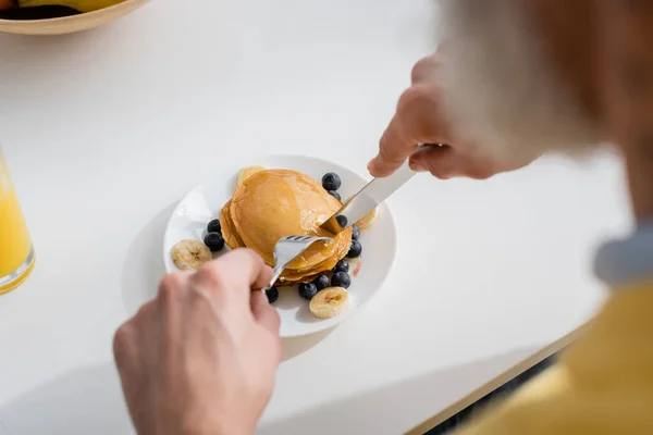 Homem desfocado cortando panquecas com frutas na cozinha — Fotografia de Stock