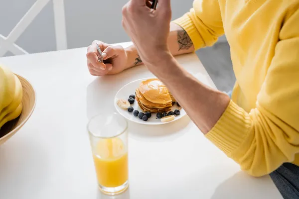 Ausgeschnittene Ansicht eines reifen Mannes mit Messer in der Nähe von Pfannkuchen und Orangensaft in der Küche — Stockfoto
