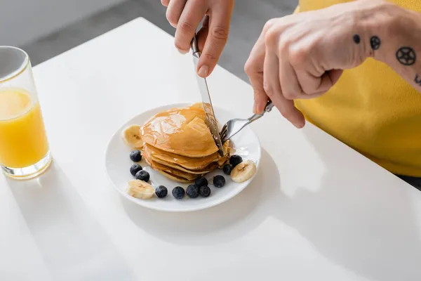 Cropped view of man cutting pancakes near berries and banana at home — Stock Photo