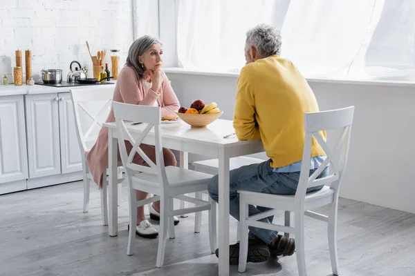 Mature woman looking at husband near breakfast in kitchen — Stock Photo
