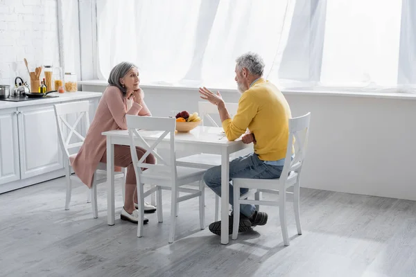 Зрелая пара разговаривает рядом с фруктами на кухне дома — стоковое фото