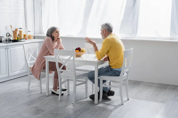 Pareja madura hablando cerca de frutas en la cocina en casa - foto de stock