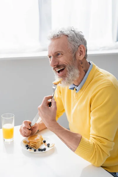 Hombre sonriente comiendo deliciosos panqueques en la cocina - foto de stock