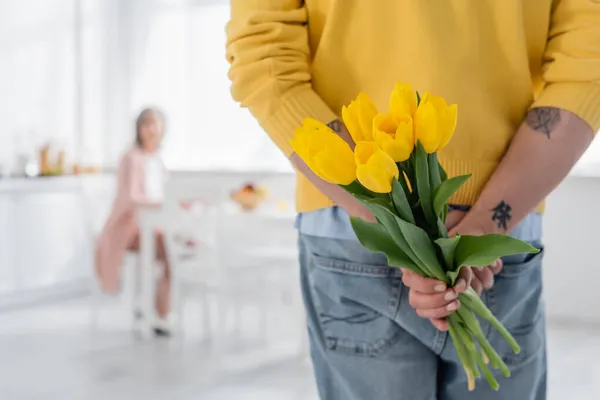 Зрілий чоловік ховає квіти біля розмитої жінки на кухні — стокове фото