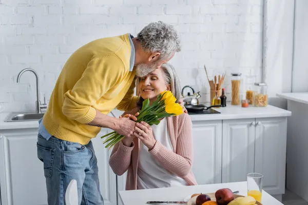 Homme présentant des fleurs à une femme souriante près des fruits dans la cuisine — Photo de stock