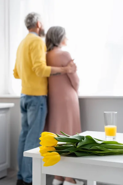 Tulipes sur la table près du couple flou dans la cuisine — Photo de stock