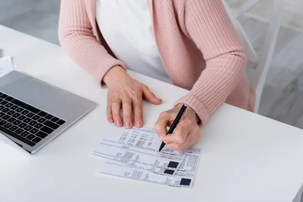 Vista ritagliata della donna che scrive sulla fattura vicino al computer portatile a casa — Foto stock