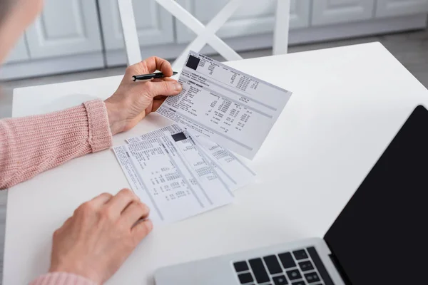 Cropped view of woman holding papers with bills near laptop with blank screen at home — Stock Photo