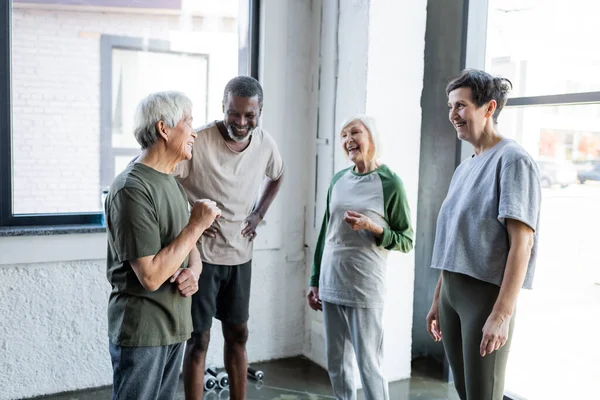 Positive interracial senior people in sportswear talking in gym — Stock Photo