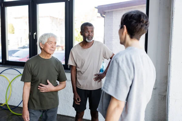 Hombres mayores multiétnicos mirando a la deportista en el gimnasio - foto de stock