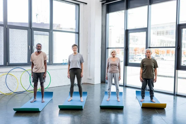 Interracial senior people in sportswear standing on fitness mats in gym — Stock Photo