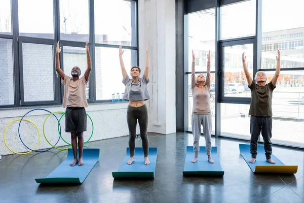 Multicultural senior people practicing yoga in mountain pose on fitness mats in sports center — Stock Photo