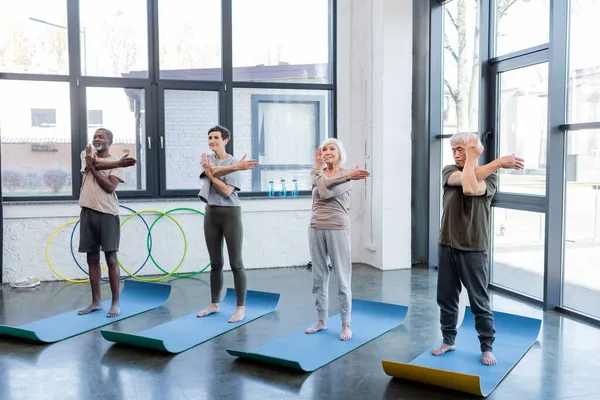 Personas mayores multiculturales que practican yoga en esteras en un centro deportivo - foto de stock
