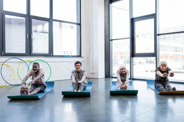 Lächelnde interrassische Menschen dehnen sich während der Arbeit im Fitnessstudio — Stockfoto