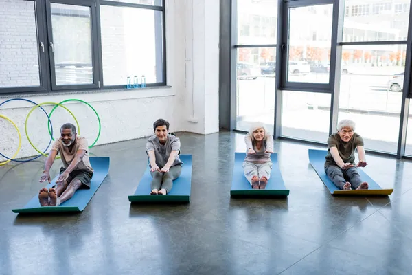 Anziani interrazziale persone riscaldamento su fitness stuoie in palestra — Foto stock