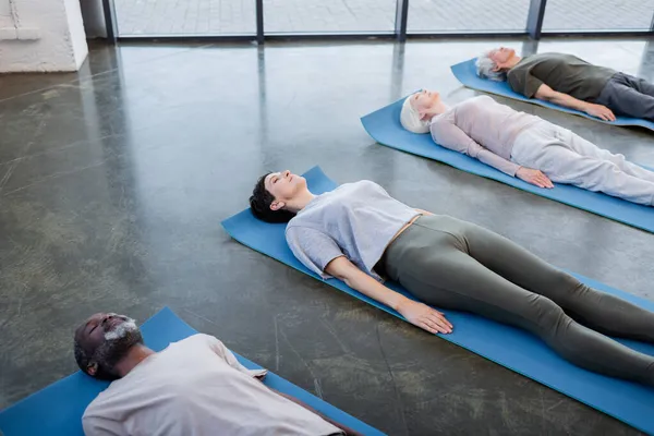 High angle view of multiethnic senior people lying on yoga mats in sports center — Stock Photo