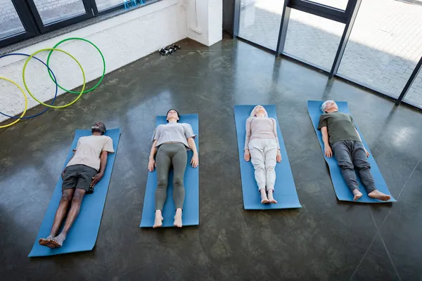 Vue du dessus des personnes âgées multiculturelles allongées sur des tapis de yoga dans la salle de gym — Photo de stock