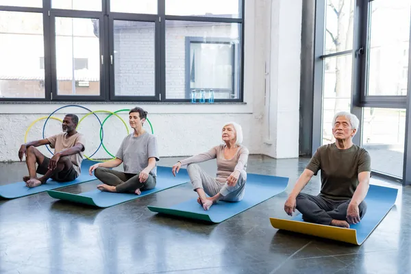 Personnes âgées multiethniques pratiquant le yoga dans un centre sportif — Photo de stock