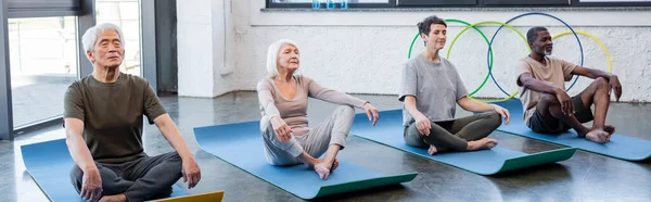 Interracial senior people with closed eyes meditating in sports center, banner — Stock Photo
