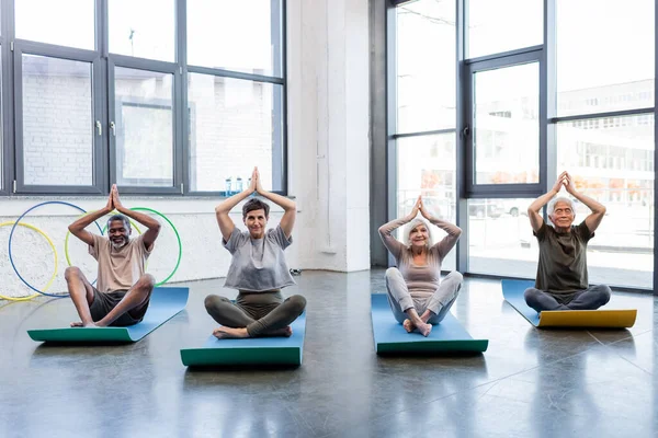 Sorridente interrazziale anziani che praticano yoga nel centro sportivo — Foto stock