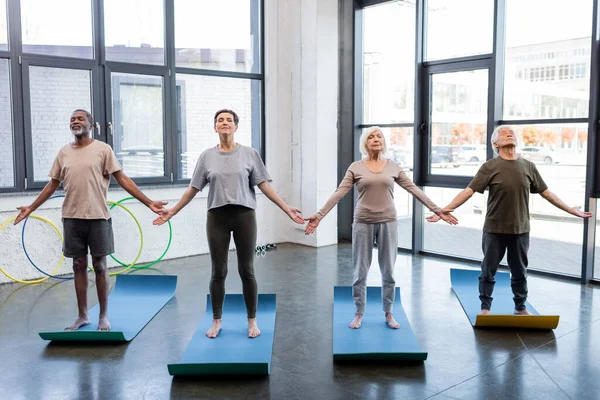 Personas mayores multiétnicas de pie en yoga posan en el gimnasio - foto de stock