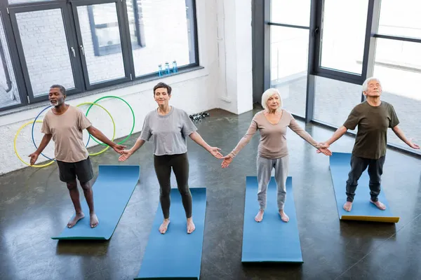 Високий кут зору міжрасових літніх людей, що стоять в позі йоги в спортивному центрі — стокове фото