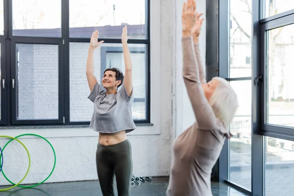 Glückliche Seniorin übt sich in Berg-Pose neben verschwommenem Freund im Sportzentrum — Stockfoto