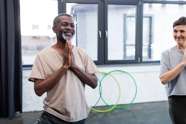 Sorridente uomo afro-americano che pratica yoga vicino ad un amico anziano nel centro sportivo — Foto stock