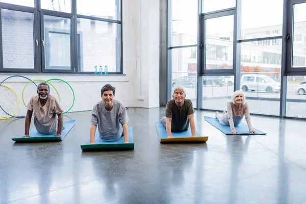 Smiling multicultural senior people looking at camera on yoga mats in sports center - foto de stock