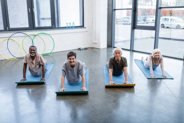 Group of positive interracial people looking at camera while practicing cobra pose in sports center — Stock Photo