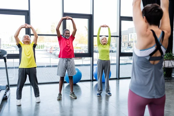Smiling multicultural people exercising near blurred trainer in gym — Stock Photo