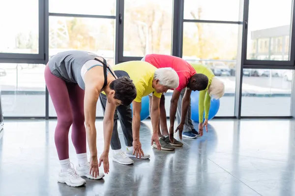 Group of multiethnic people stretching together in gym — Stock Photo