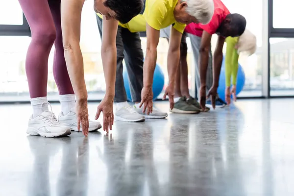 Donna anziana che si estende vicino ad amici multietnici offuscati nel centro sportivo — Foto stock