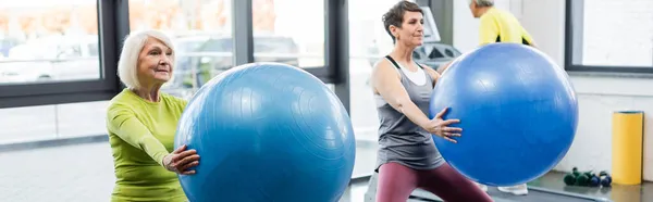 Deportista de pelo gris sosteniendo pelota de fitness en el centro deportivo, pancarta - foto de stock