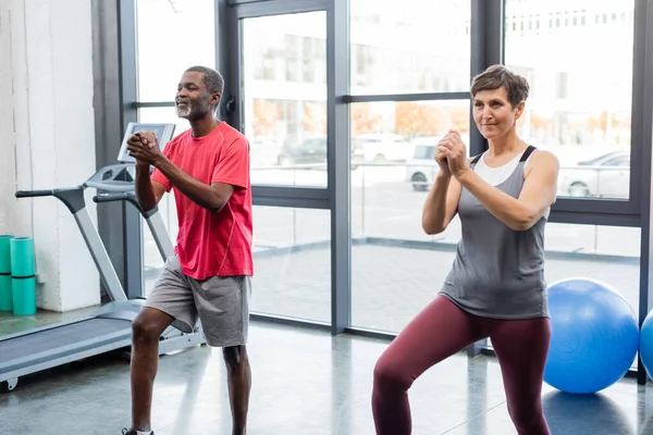 Entrenamiento de personas interraciales cerca de equipos deportivos en gimnasio - foto de stock