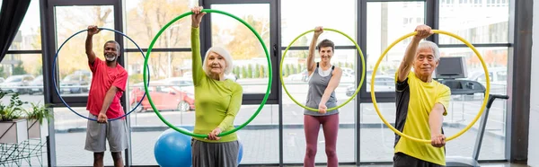 Group of multiethnic elderly people training with hula hoops in sports center, banner — Stock Photo