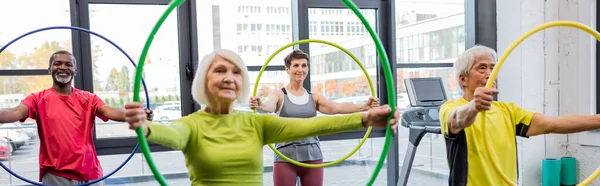 Smiling multicultural people exercising with hula hoops in gym, banner — Stock Photo