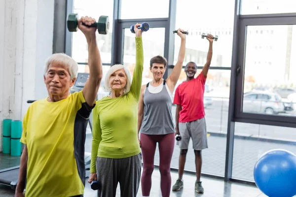 Group of interracial senior people exercising with dumbbells in sports center — Stock Photo