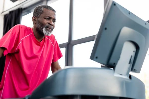 Entrenamiento de deportista afroamericano enfocado en cinta de correr borrosa en gimnasio - foto de stock