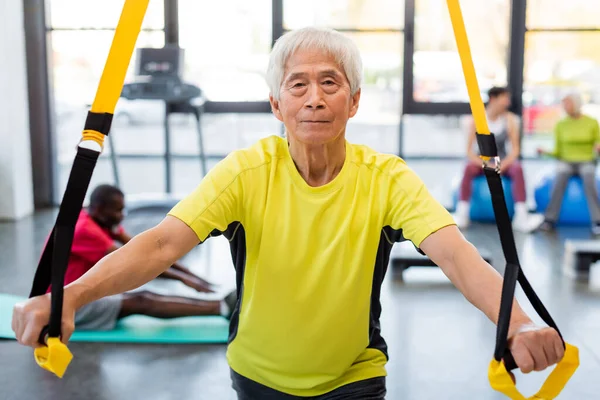 Elderly asian sportsman training with resistance band in sports center — Stock Photo