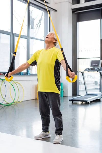 Elderly asian sportsman training with resistance band in gym — Stock Photo