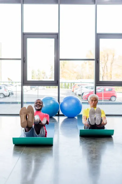 Des sportifs multiethniques souriants s'entraînent sur des tapis de fitness dans une salle de sport — Photo de stock