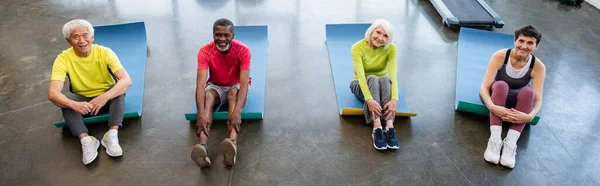 High angle view of smiling interracial senior people looking at camera on fitness mats in gym, banner — Stock Photo