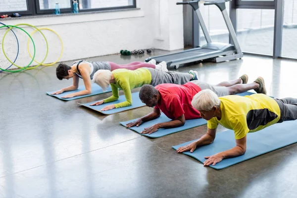 Anziani multietnici in piedi in tavola su tappeti fitness — Foto stock