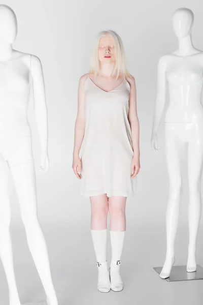 Повна довжина моделі альбіно в сукні, що стоїть біля манекенів на білому тлі — стокове фото
