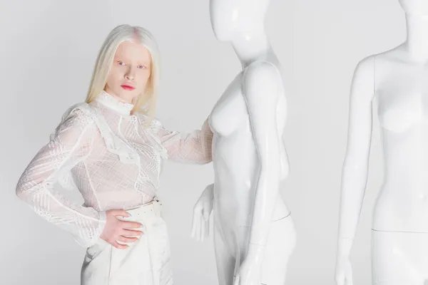 Mulher loira elegante segurando a mão no quadril perto de manequins isolados no branco — Fotografia de Stock