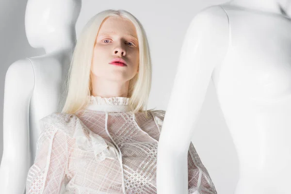 Молода альбіносова жінка в модній блузці дивиться на камеру біля манекенів на білому тлі — стокове фото